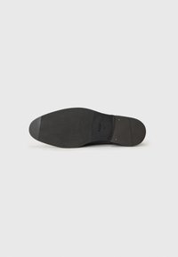 Sort lædersål med en glat finish, rund tå og tekstureret gummisål. Udstyret med guldfarvet hardware og præget branding.