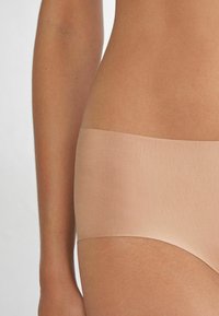 Beige naadloze slipjes met een zachte textuur en een gemiddelde hoogte, voorzien van een brede elastische tailleband en geen zichtbare naden.