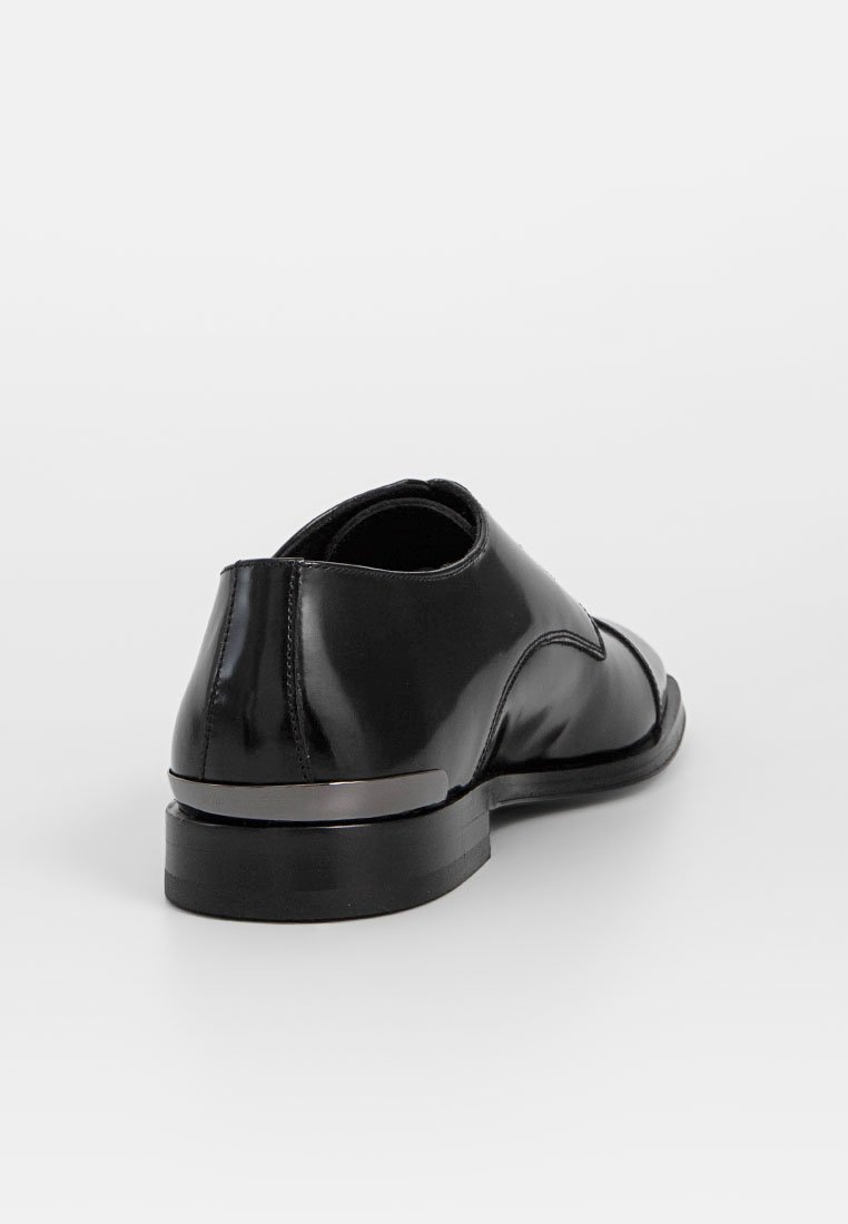 Schwarzer Lederschuh mit glänzendem Finish, runder Form und niedrigem Absatz. Besitzt ein elegantes Design mit dezenten Nähten und einem metallischen Akzent.