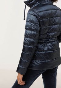 Chaqueta puffer azul marino con un acabado brillante, diseño de costura horizontal, capucha ajustable y detalle de cintura elástica.
