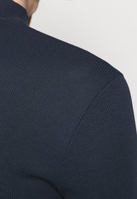 Maglione a collo alto a costine di colore navy, caratterizzato da un design aderente, tessuto testurizzato e un'apertura del collo liscia per un comfort aggiuntivo.