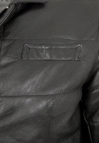 Schwarze Lederjacke mit strukturiertem Finish, auffälliger Naht und einer kleinen, rechteckigen Pattentasche auf der linken Seite.