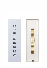 Montre dorée avec un cadran carré blanc et un bracelet à maillons, présentée dans une boîte blanche arborant le nom de la marque "ROSEFIELD" sur le côté.