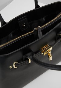 Svart läder toteväska med guldfärgad hårdvara, med ett zippered fack, en strukturerad form och dubbla handtag för bärande.