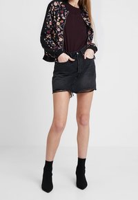 Sort blomsterbomberjakke med lange ærmer, parret med en sort denim-miniskirt med frynset kant, og sorte ankelstøvler.