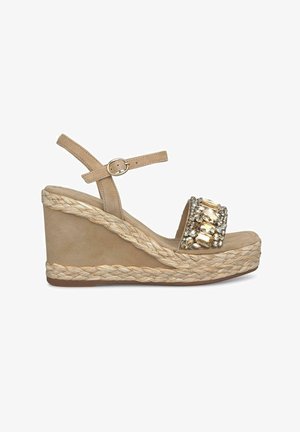 Beige wedge sandal with a textured jute sole, adorned with a jeweled strap and a buckle detail. Smooth material and open toe design.