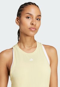 Top atlético sin mangas de color amarillo claro con cuello redondo, que presenta una capa interior blanca y un pequeño logo blanco en el pecho.