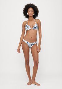 Bikini komplektas su trikampiu viršutiniu ir atitinkamu apatinio maudymosi kostiumėlio dalimi, su baltu pagrindu ir mėlynu gėlių raštu. Medžiaga atrodo lygi, su reguliuojamomis juostelėmis.