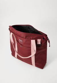 Bordeaux nylon totebag med rosa webbing-håndtak, glidelås-lukking og utvendig lomme. Innvendig har den en svart foring.