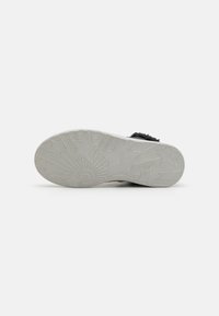Suela de zapato de goma en gris claro con patrones de estrellas y explosiones de sol, presentando un acabado texturizado y bordes curvados para mayor tracción.