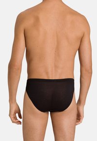 Schwarze Baumwollslips, körperbetontes Design, elastischer Bund, glatte Textur, minimale Bedeckung und ohne Muster. Von hinten betrachtet.