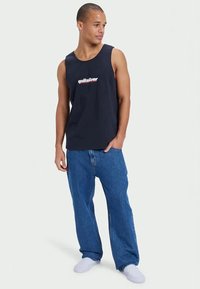 Navy tank top with white and red "Quiksilver" logo, paired with loose denim jeans and white socks. Simple design, regular fit.