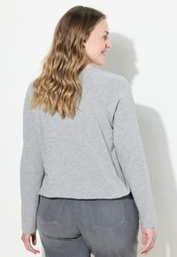 Lichtgrijs langemouwen T-shirt met een afgeronde zoom en raglanmouwen, gemaakt van zachte, textuurstof. Zichtbare stikseldetails.