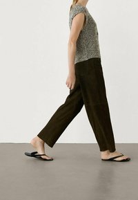 Top a maniche corte grigio e nero lavorato a maglia abbinato a pantaloni a gamba larga marrone scuro e infradito nere, che cammina su una superficie neutra.