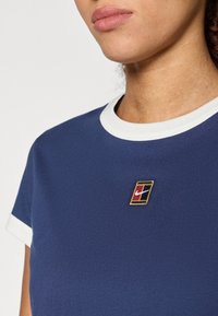 Ναυτικό μπλουζάκι με λευκό ριμπ κολάρο, διακοσμημένο με ένα κεντημένο πολύχρωμο λογότυπο στο στήθος και κοντά μανίκια.