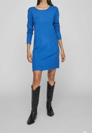 Robe en tricot bleue à manches longues, décolleté rond et poignets côtelés. Associée à des bottes en cuir noir hautes. Design simple et ajusté.