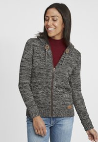 Grå stickad zip-up hoodie med ett strukturerat mönster, träknappar och en figursydd design. Bärs över en bourgognefärgad polotröja, tillsammans med jeans.