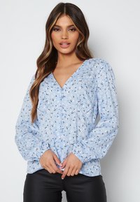 Blusa blu chiaro con piccola stampa floreale, scollatura a V, maniche lunghe a sbuffo e dettagli con bottoni sulla parte anteriore. Tessuto morbido e leggero.