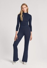 Granatowy bodysuit z długim rękawem i wysokim dekoltem, w połączeniu z dopasowanymi spodniami dzwonami. Gładka tekstura materiału i dopasowany krój.