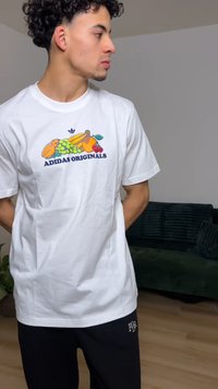 Baltas medvilninis marškinėlis su spalvingu vaisių paveikslėliu ir užrašu „ADIDAS ORIGINALS“. Trumpomis rankovėmis ir apvalia iškirpte.