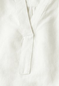 Vêtement en lin blanc avec un décolleté en V deep, présentant des coutures subtiles et une surface légère et texturée pour une meilleure respirabilité.