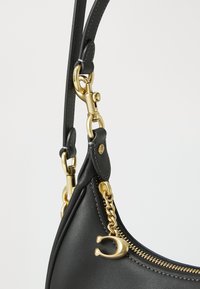 Sac à main en cuir noir avec un design courbé, quincaillerie dorée, fermeture à glissière et un détail en chaîne pour une texture supplémentaire.