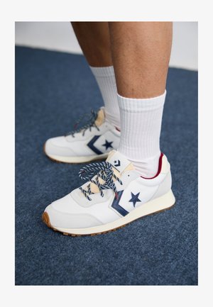 Witte en marineblauwe sneaker met een gestructureerd bovenwerk, sterlogo, patronen op de veters en een rubberen zool, gecombineerd met witte geribbelde sokken.