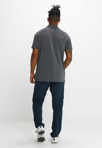 Polo grigio con maniche corte, abbinato a pantaloni blu navy. L'outfit presenta un tessuto leggero e una vestibilità comoda, adatto per un abbigliamento informale.