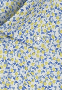 Camicia colletto in tessuto bianco con un motivo floreale che presenta limoni gialli e foglie blu, accentuata da un singolo bottone bianco.