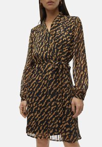 Robe portefeuille en tissu noir transparent avec imprim�é animal marron. Manches longues, taille marquée avec un lien, et une jupe fluide.