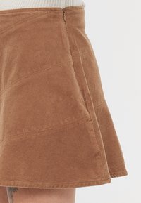 Bruine corduroy rok met een uitlopende silhouet, voorzien van een verticale ribbeltextuur, een zijrits en gestikte panelen voor extra detail.