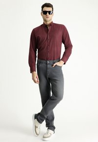Camisa de rayas rojas y marino de manga larga con diseño de botones, combinada con jeans grises y zapatillas blancas con acentos verdes y beige.