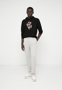 Felpa nera con un design grafico colorato, abbinata a pantaloni della tuta grigi chiari e sneakers bianche con dettagli beige.