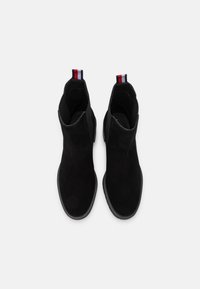 Botas de tobillo de ante negro con un diseño elegante, puntera redondeada y tiradores en la parte trasera en contraste rojo y azul. Suela de goma flexible.