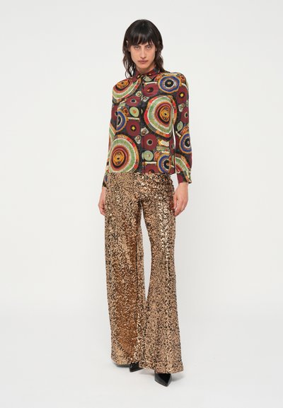 Multikleurige gestreepte blouse met lange mouwen, gecombineerd met wijde paillettenbroek in goud. De outfit heeft een glanzende textuur en levendige kleuren.