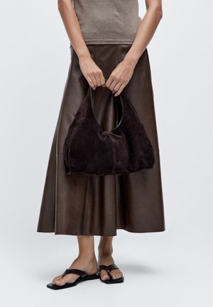 Bruine suede schoudertas met een zachte, gebogen vorm. Glad oppervlak, minimalistische stiksels en een korte handgreep voor gemakkelijk dragen.