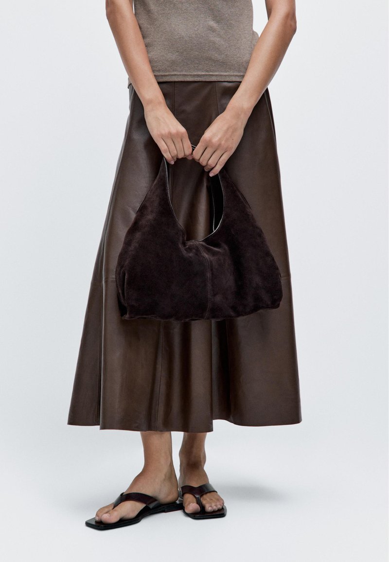 Brown suede shoulder bag with a soft, curved shape. Smooth texture, minimal stitching, and a short handle for easy carrying.