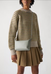 Liten, strukturerad crossbody-väska i mjukt, ljusgrönt läder med en jämn textur, som har en elegant design och justerbar rem.