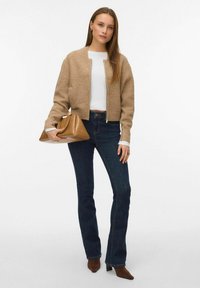 Gai brūnās krāsas apgriezts kardigans ar rāvējslēdzēju priekšā, balta krekla apakšā, tumši zila plati uzsistās džinsi un brūna rokassoma. Brūni papēžu apavi.