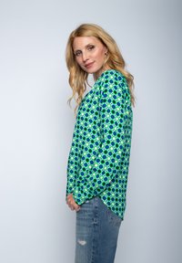 Bluzka z długim rękawem w niebiesko-zielonym kolorze z okrągłym wzorem. Charakteryzuje się luźnym krojem i rozcięciami po bokach dla swobody ruchów.