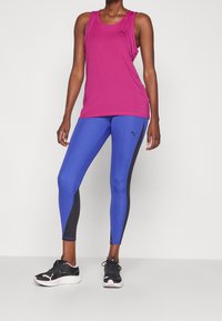Rosa idrottstopp och blå leggings med svarta detaljer. Tillverkad av stretchigt material, med rund halsringning och figurnära design. Svarta sneakers.