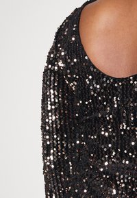 Robe noire à sequins avec un dos ouvert, dotée d'un col arrondi et d'une surface texturée composée de sequins réfléchissants superposés.