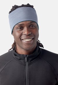 Bandeau de sport bleu en tissu extensible, avec une texture lisse. Porté par une personne dans une veste noire zippée.