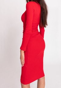 Robe rouge côtelée ajustée avec des manches longues, longueur genou, encolure ronde et texture froncée mettant en valeur la silhouette.