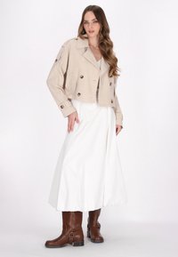 Beige cropped jakke med dobbeltknap lukning og forlommer, båret over en hvid nederdel og brune læder ankelstøvler.
