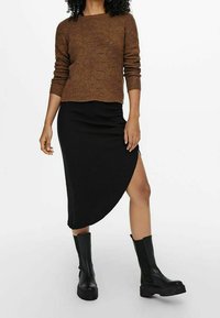 Pull en maille marron à manches longues, associé à une jupe midi noire côtelée avec une fente haute et des bottes noires épaisses montant jusqu'aux genoux.