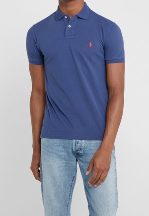 Polo shirt bleu en coton, à manches courtes, avec un boutonnière à deux boutons et un petit logo rouge brodé sur la poitrine gauche.