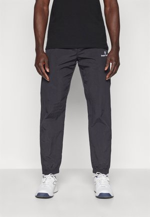 Black, lightweight, synthetic track pants with elastic cuffs; features branded logo on front. Worn with white athletic shoes.