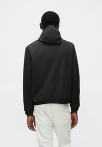 Μαύρο μπουφάν με κουκούλα, ελαστικά μανίκια και τελείωμα, κατασκευασμένο από λείο, ελαφρύ υλικό. Άσπρο παντελόνι εμφανίζεται κάτω από το τελείωμα του μπουφάν.