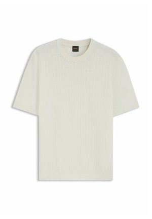 Pull en maille crème à manches courtes avec un subtil côtes verticales et un col rond, doté d'une petite étiquette noire au niveau du col.